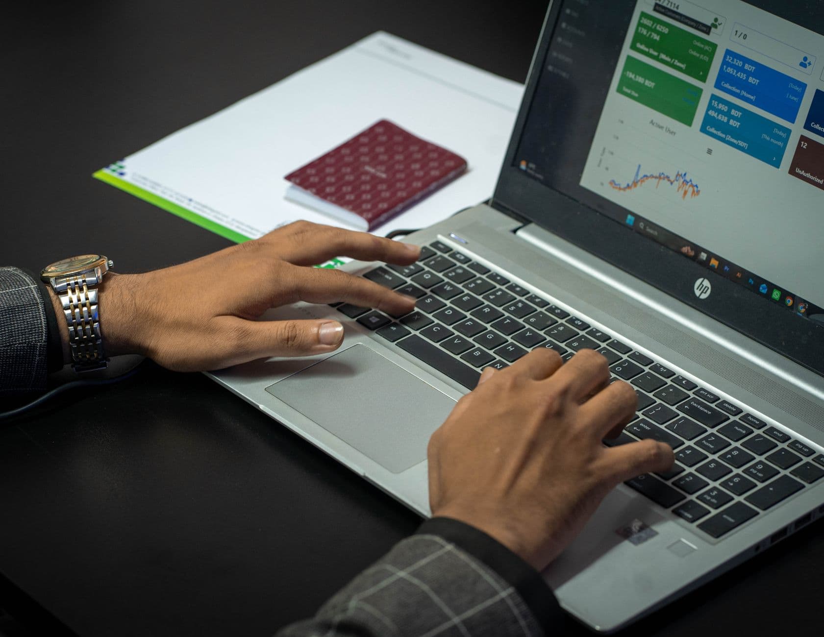 Mains posées sur un clavier d'ordinateur portable avec un tableau de bord financier affiché à l'écran, lumière naturelle de côté